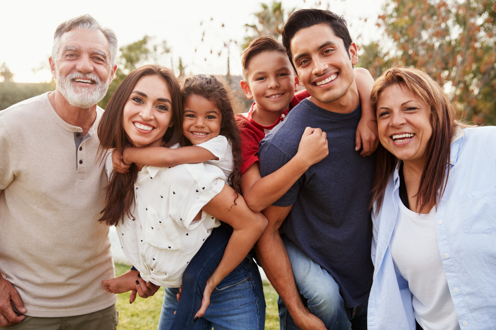 Three,Generation,Hispanic,Family,Standing,In,The,Park,,Smiling,To